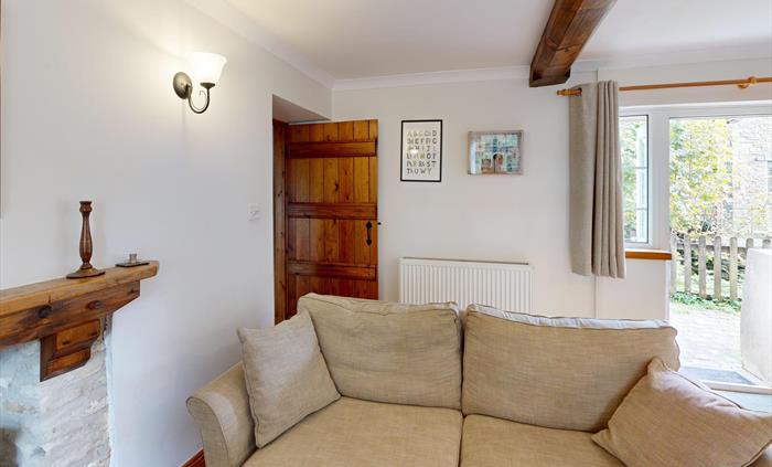 The inviting living room of Ty Cerbyd with light neutral furnishings, rustic wooden beams, and a door opening onto the garden.